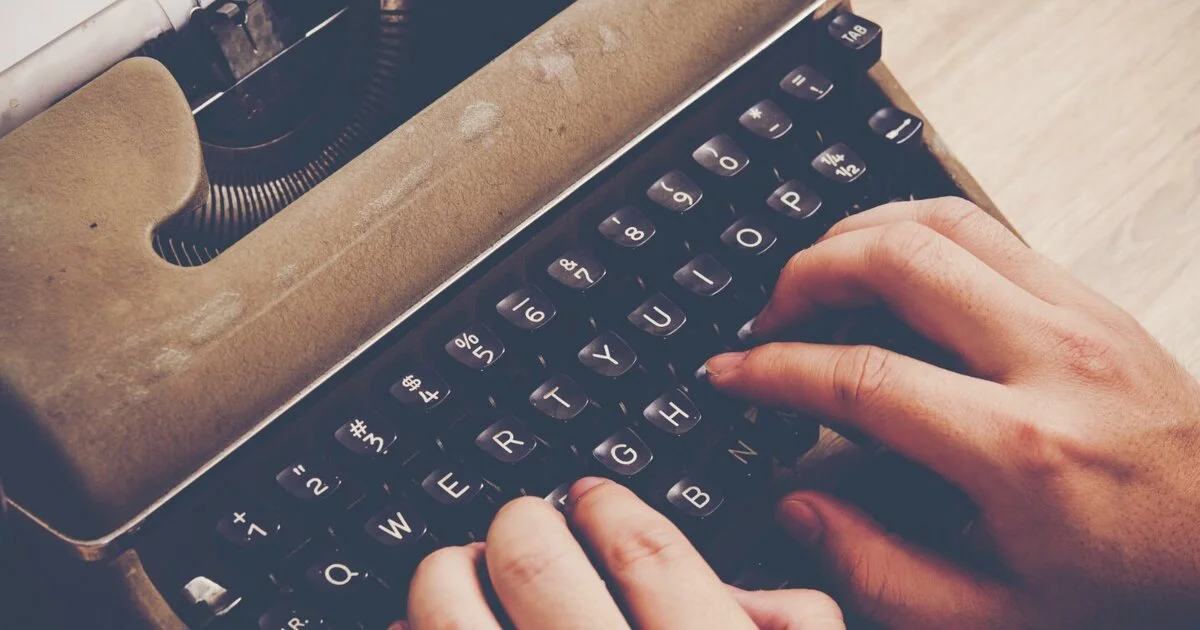 Image of an author typewriting on an old manual typewriter, using both hands.