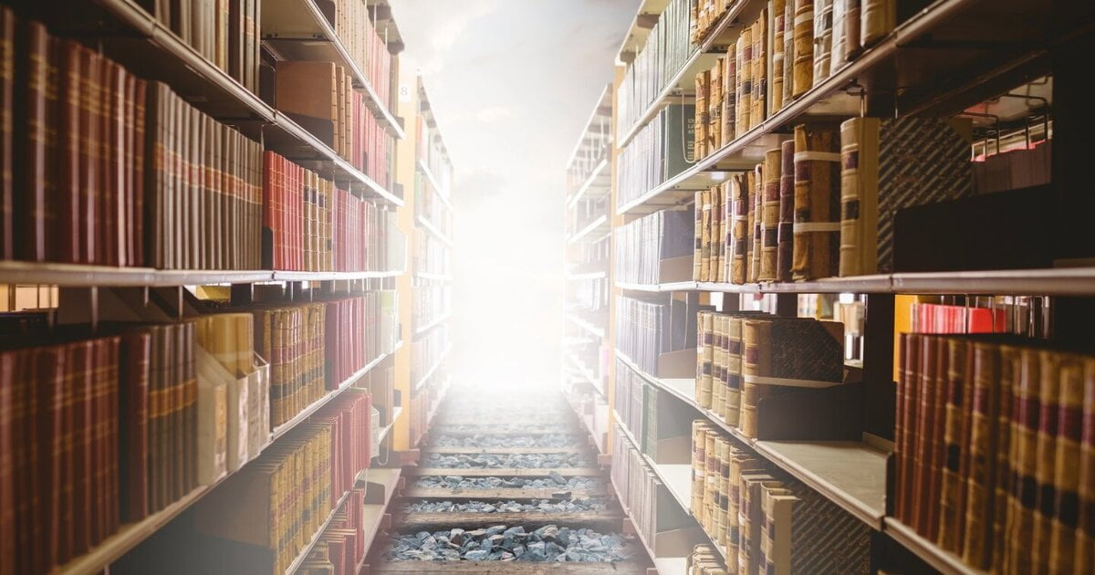 Fiction novels image of two large rows of book cases, which are stacked with books. There is a railroad going through the middle of the image to a white light.