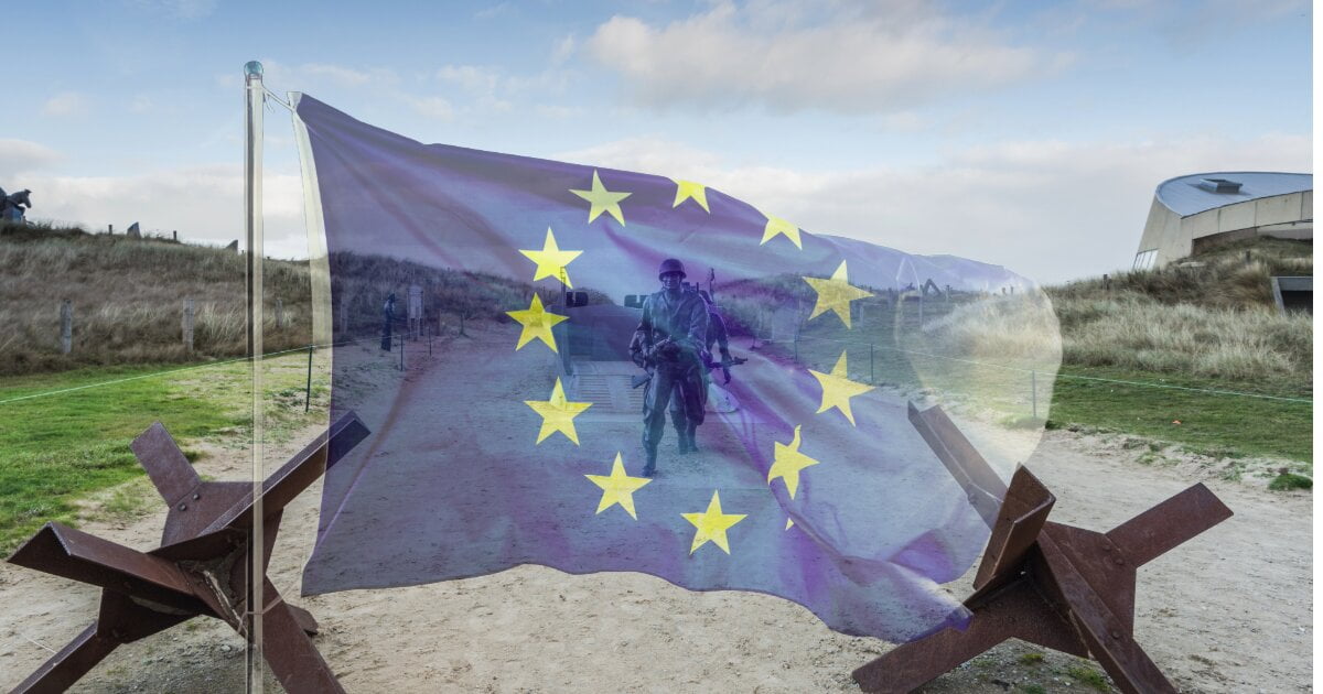 D-Day landing statue on the beach at Normandy, with the opague flag of the EU, and stars of the flag circling the bronze American Solder depicted in the statue.