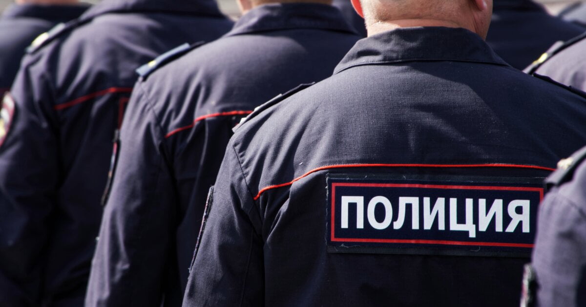 Image of the backs of Russian Policemen in formation, but stationary in ranks of three. Their backs have a sign saying "Police" in Russian on them.