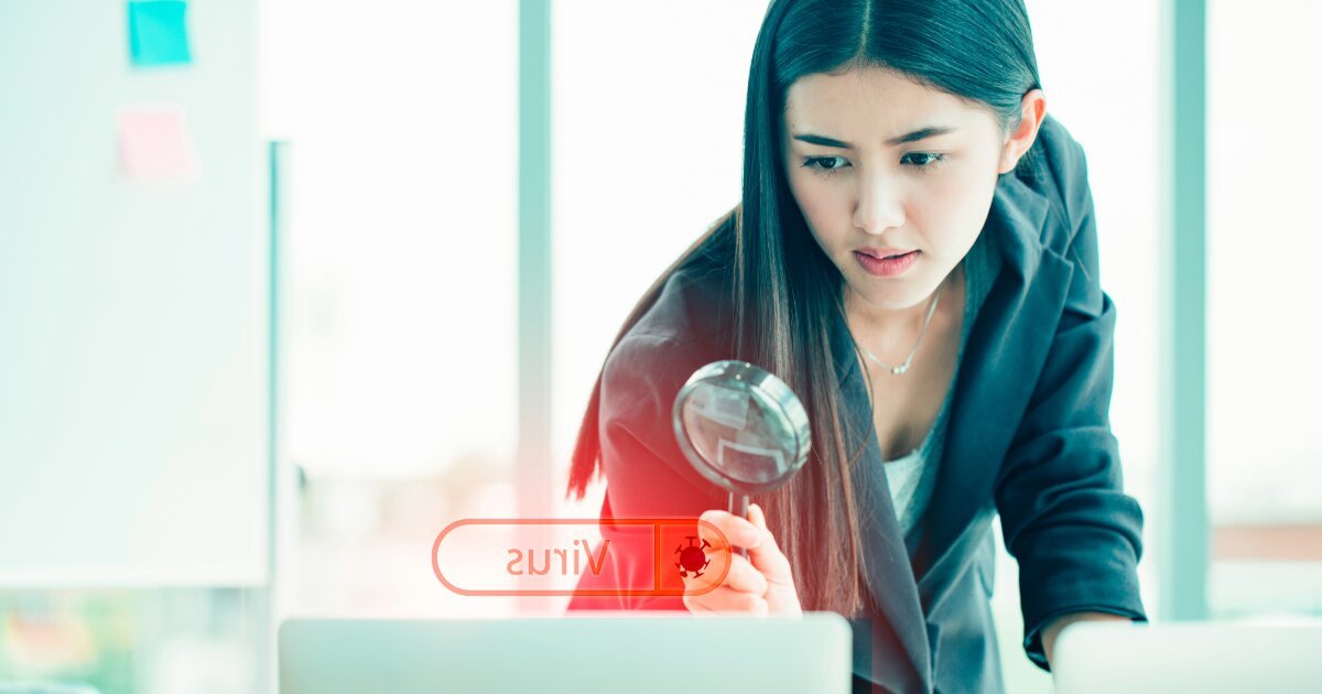 A young woman in a business suit standing over a laptop with a magnifying glass reading the red image, Spyware.