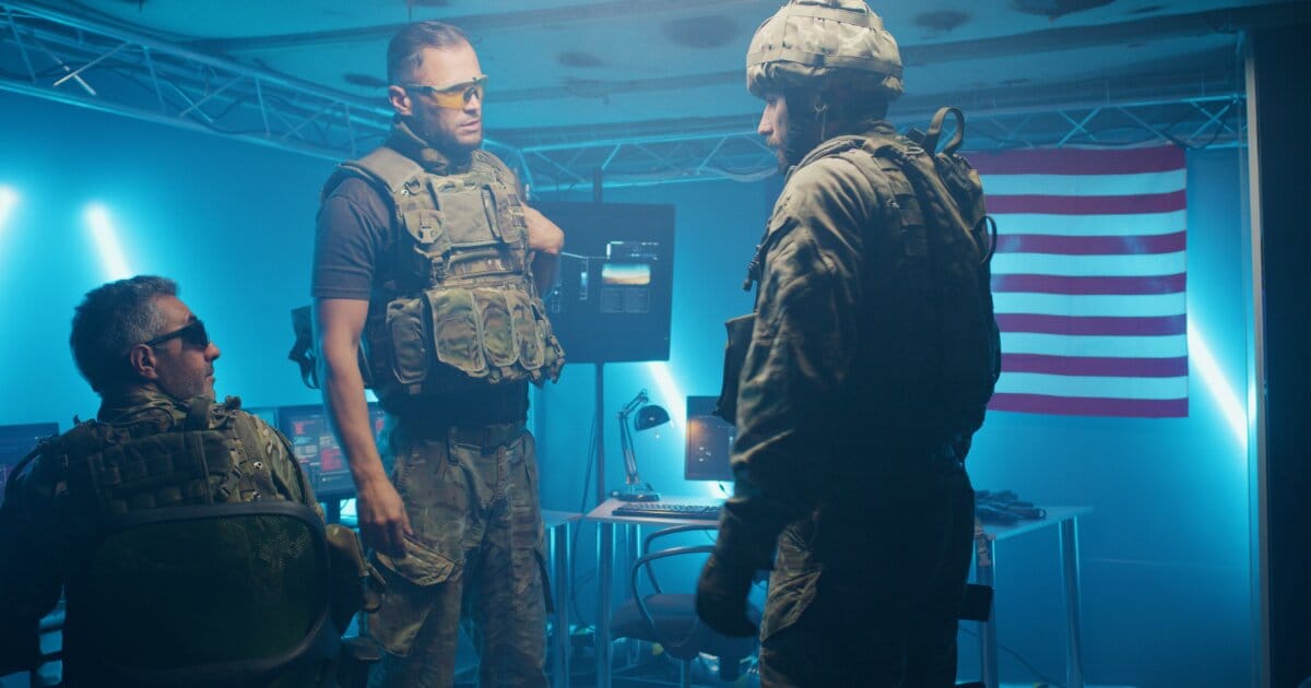 Three private intelligence tactical-operators inside a mobile tactical command center. They have military patterned body armor and combat pants.