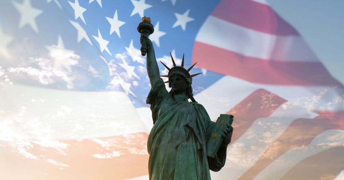 Lady Liberty is pictured in forfront with an opague blend of a blue sky blended into the American flag waving in the background.