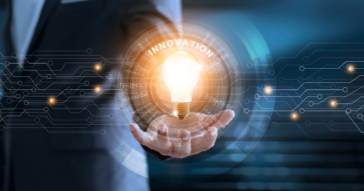 Background is a businessman in a suit holding a lightbulb which is shining into a forground digital circuit radiating different terms including the title named Innovation.
